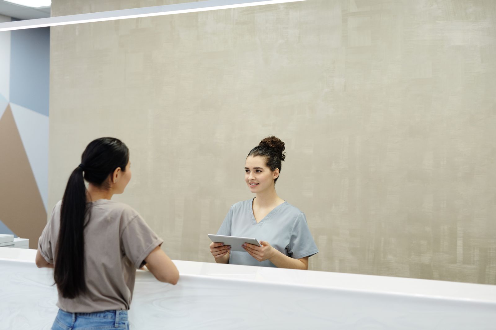 A smiling healthcare receptionist helping a visitor at the front desk