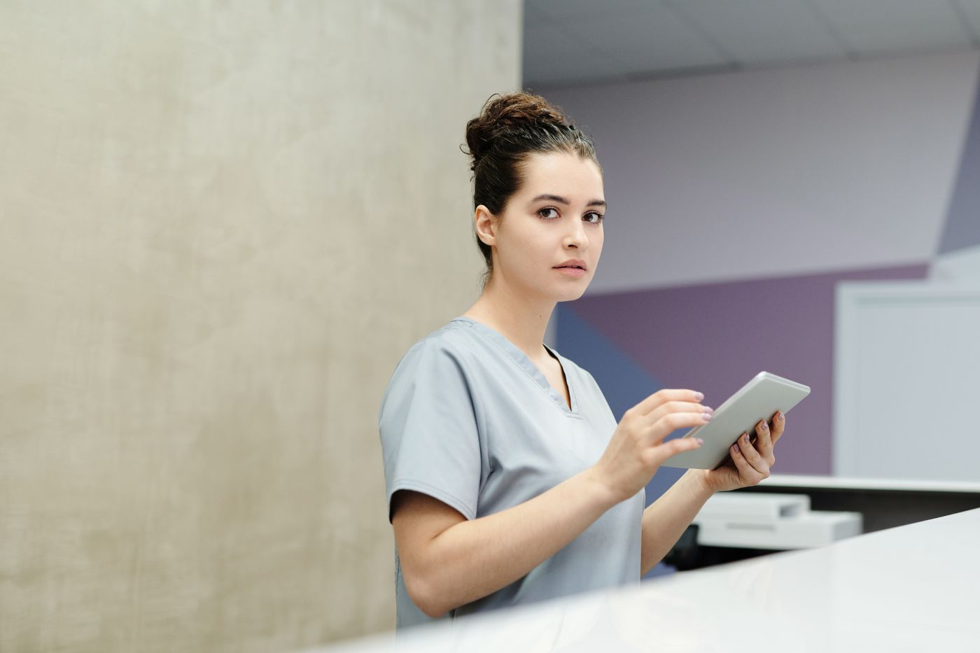 A smiling receptionist holding a tablet at a clinic front desk